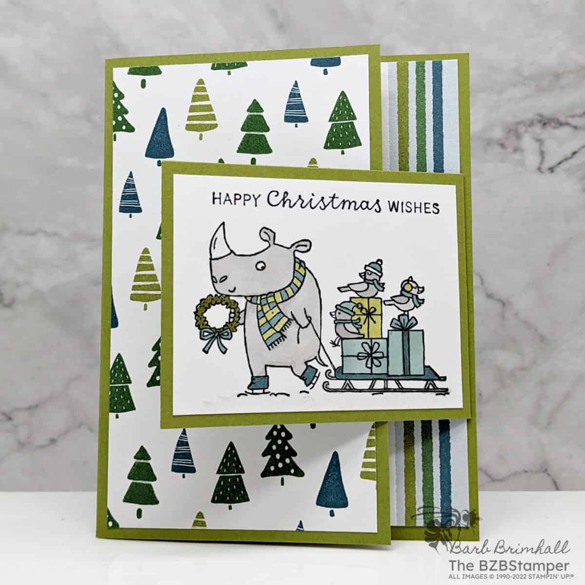 Christmas card with the Festive and Fun Stamp Set by Stampin' Up! in greens and blues featuring a rhino pulling a sled with birds and presents and sentiment "Happy Christmas Wishes."