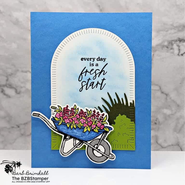 Handmade card in blues, greens and pinks featuring a wheelbarrow with flowers underneath an arch with sentiment "every day is a fresh start."