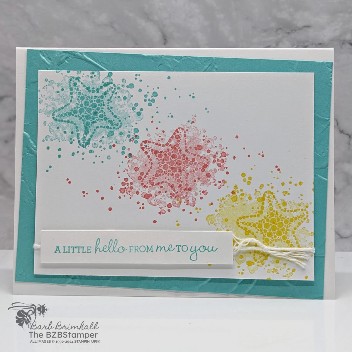 A Seaside Hello using the Sea Turtle Stamp Set with starfish seashells in blue, pink and yellow.  An embossed background and sentiment is "a little hello from me to you."