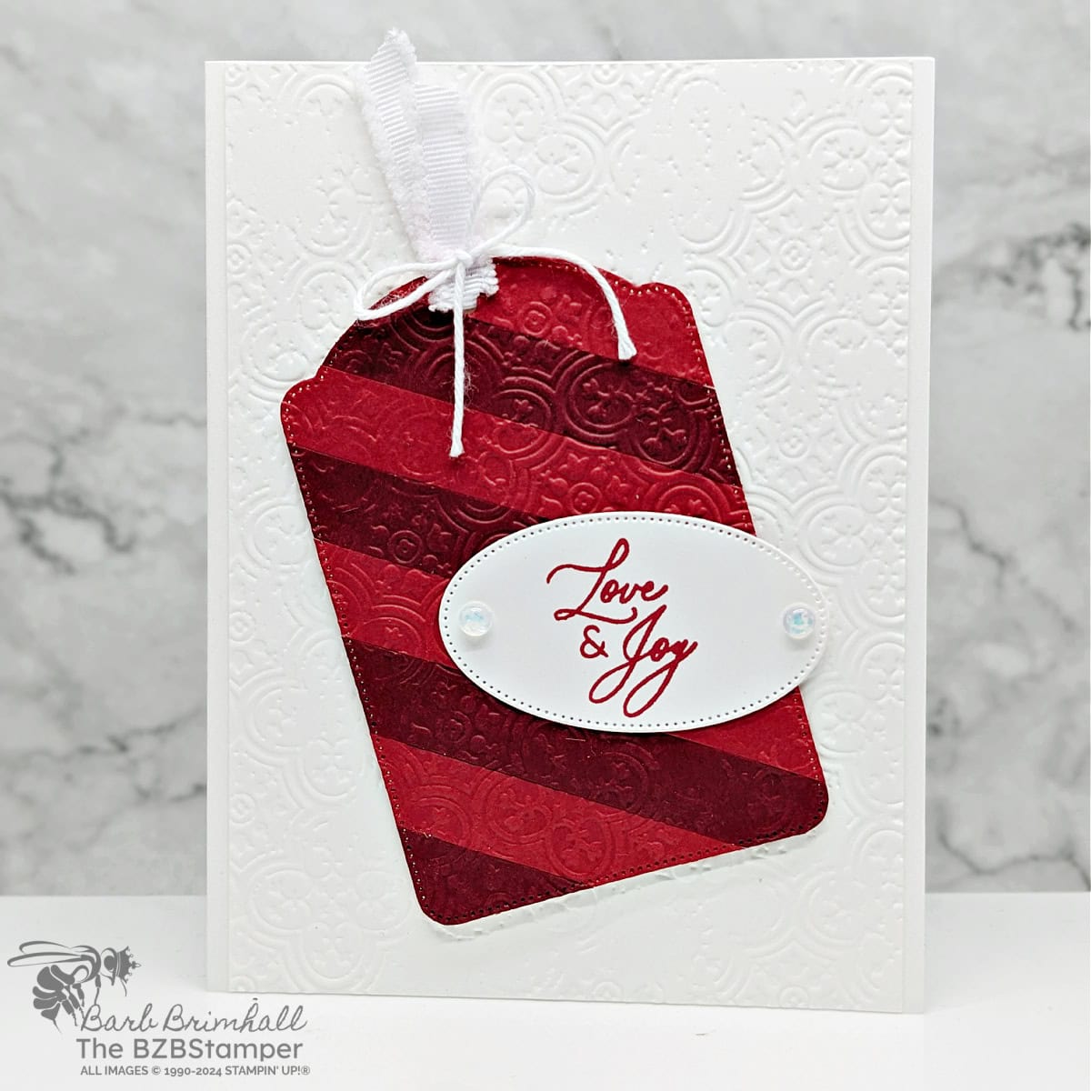 Greetings of the Season Tag Card in white and reds, with an embossed background and oval tag with "love & joy" sentiment.