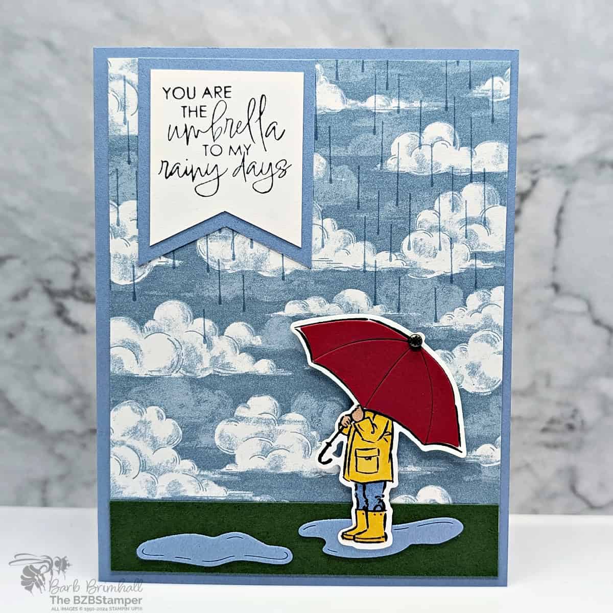 You Are the Umbrella to My Rainy Days handmade card featuring rainclouds and raindrops in blues and a person holding a red umbrella with the sentiment "you are the umbrella to my rainy days."