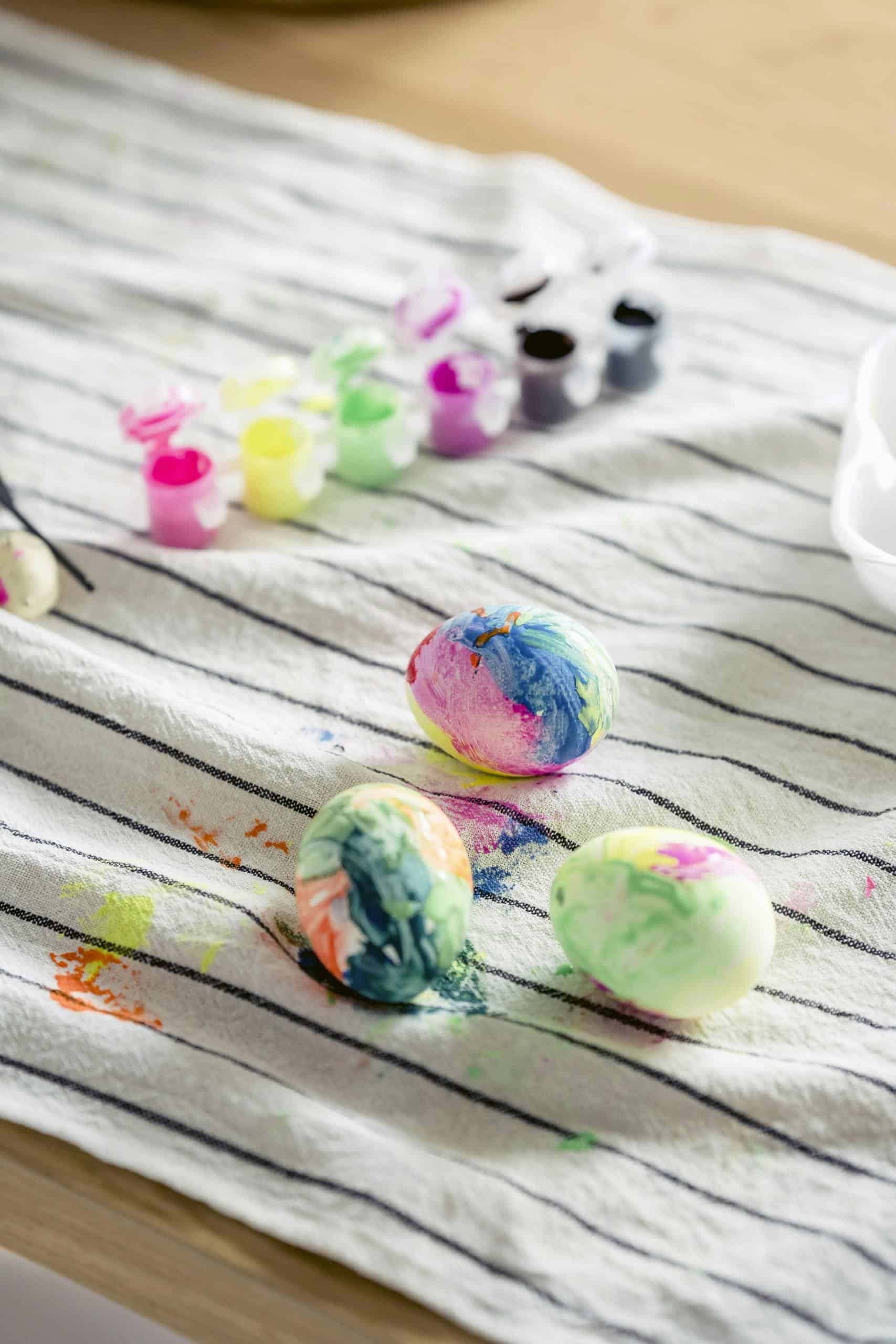 Colorful Easter eggs drying on a striped cloth with vibrant paint jars nearby, perfect for festive decor.