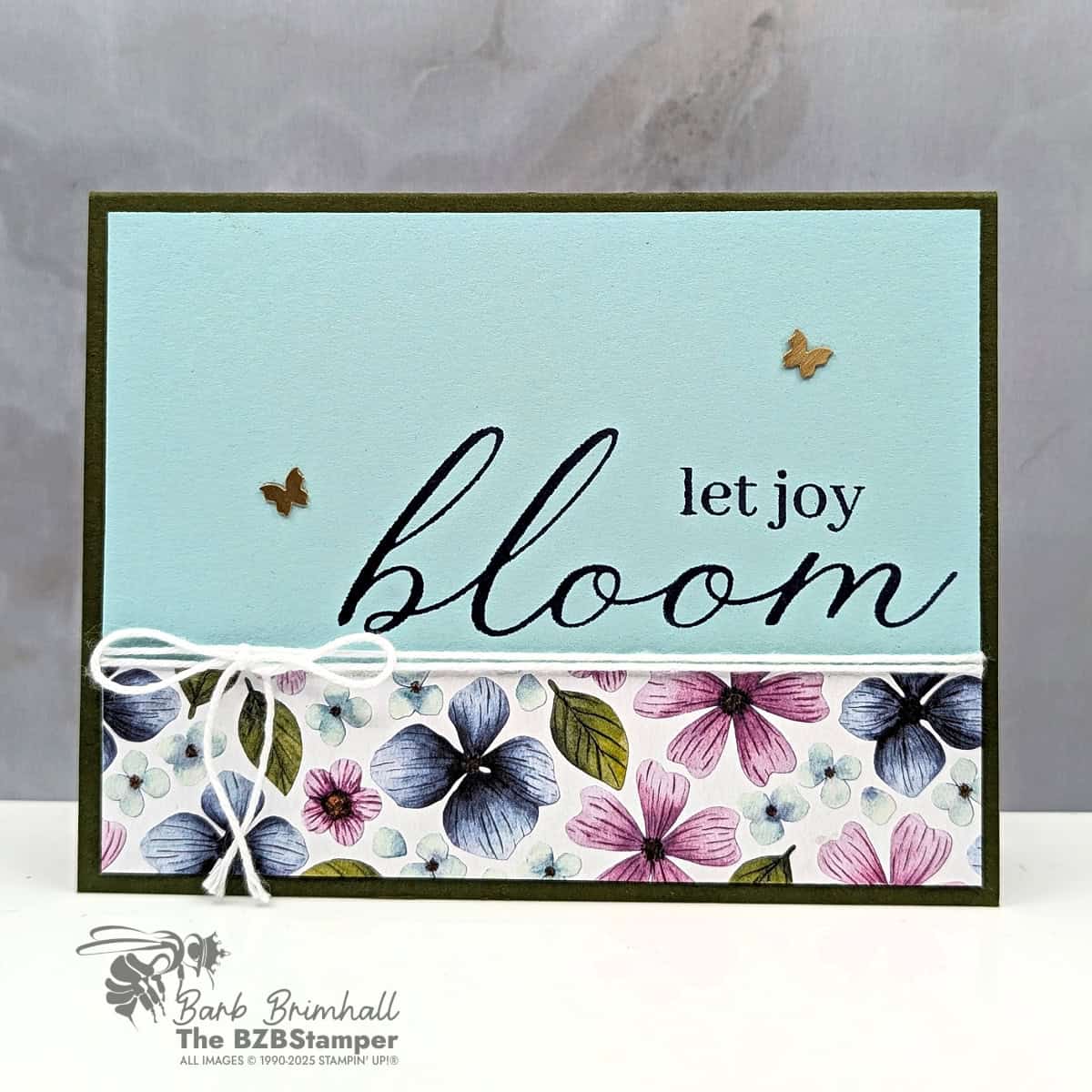 Let Joy Bloom with the Sweet Blooms Stamp Set featuring the sentiment “let joy bloom” stamped in black on a Pool Party panel. The bottom third of the card is decorated with a strip of Floral Impressions Designer Paper in pink, blue, and green tones. Embellished with White Baker’s Twine and two Brass Butterflies, layered on a Mossy Meadow card base.