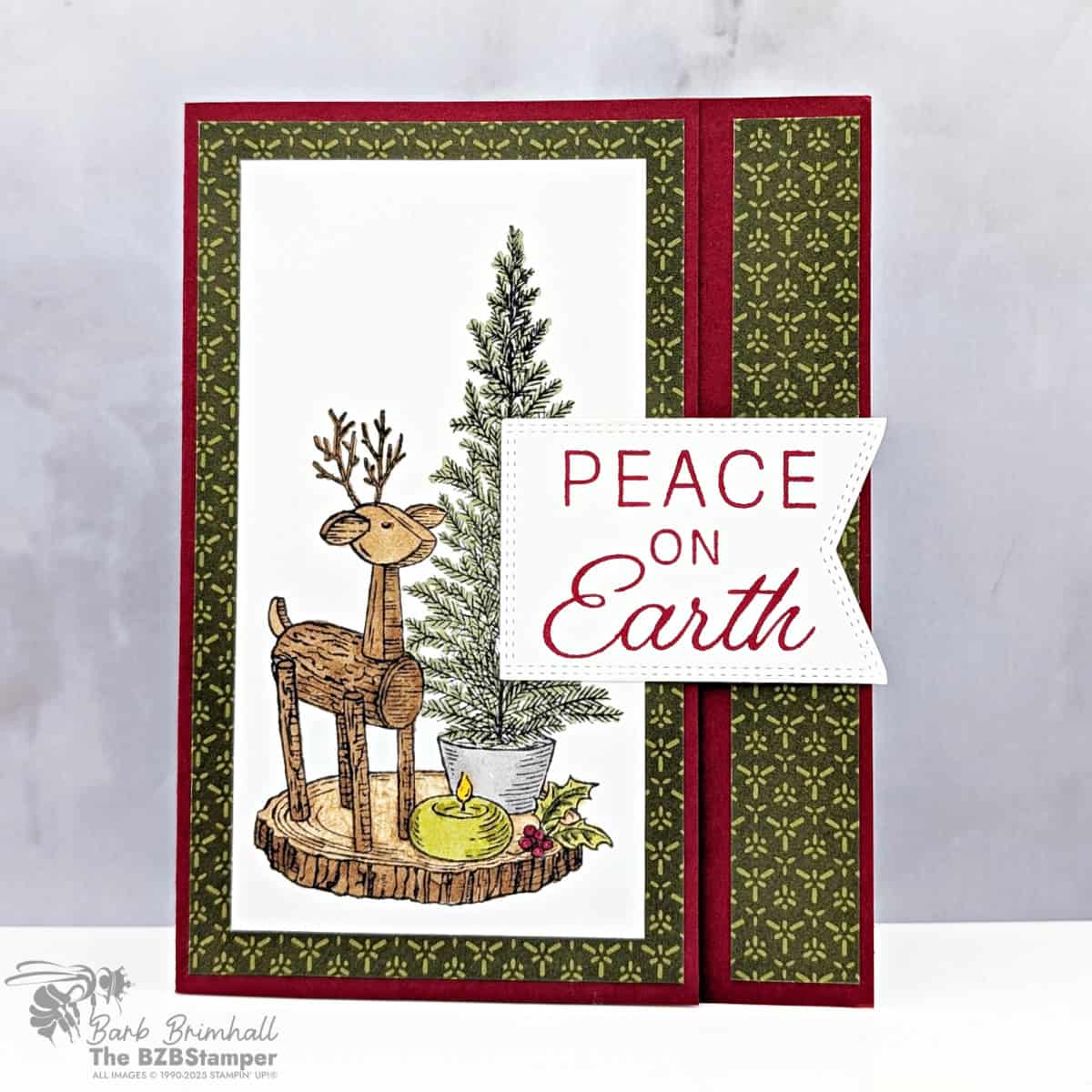 Holiday Card using the Rustic Centerpiece Stamp Set featuring a wooden reindeer and candle scene with evergreen tree, cherry cobbler cardstock, and Peace on Earth sentiment.