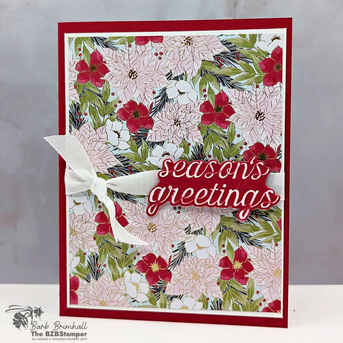 Handmade Christmas card using the Christmas Words Collage Hybrid Embossing Folder with Real Red cardstock and Traditions of Christmas Specialty Designer Paper. Features a bold die-cut “Season’s Greetings” layered over poinsettia patterned paper with a white ribbon bow.