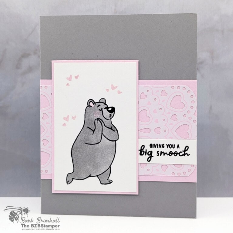 A handmade greeting card with a soft gray background and a light pink accent strip across the center. A white panel features a gray bear standing shyly with small pink hearts floating above its head. The card includes layered pink and white sections, a heart-patterned panel, and a small sentiment strip on the right, creating a sweet and gentle mood.