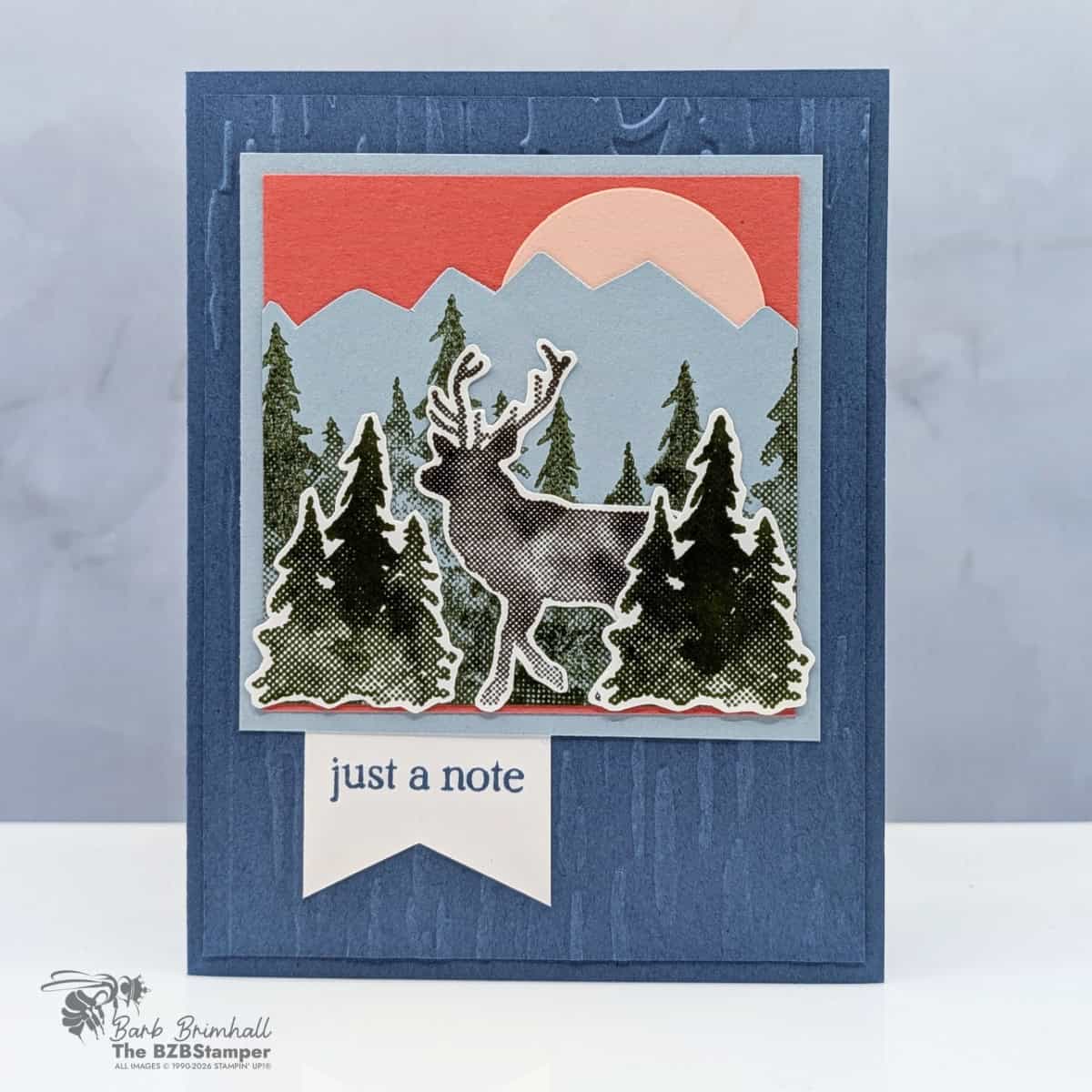 Vibrant nature-themed craft card featuring a reindeer, pine trees, mountains, and a sunset, perfect for stamping and card making.